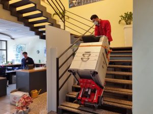 Un homme transporte la photocopieuse dans les escaliers avec le chariot d'escalier Domino